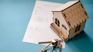 A small wooden house model and keys resting on a contract