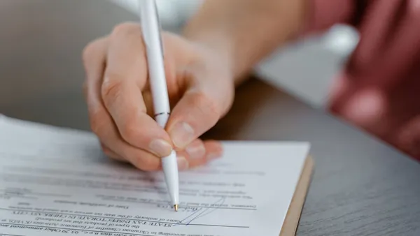 A hand signing a printed real estate agreement with a pen