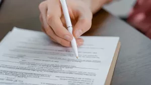 A hand signing a multi-page contract with a white pen