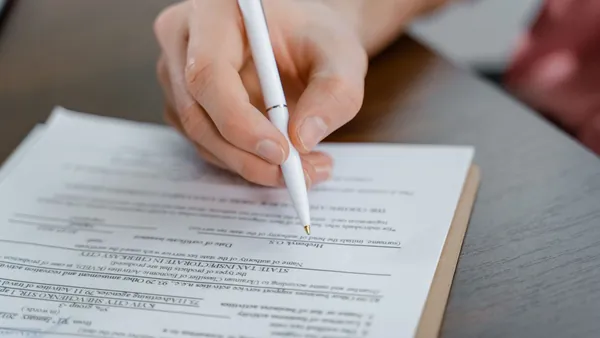 A hand signing a multi-page contract with a white pen