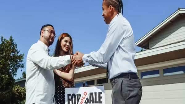 An unrelated buyer and seller shaking hands with their agent in front of a sold sign
