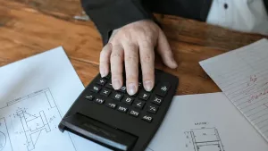 A hand using a calculator over a set of house blueprints