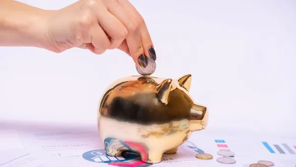 A hand dropping a coin into a house-shaped piggy bank - how to save money buying a house