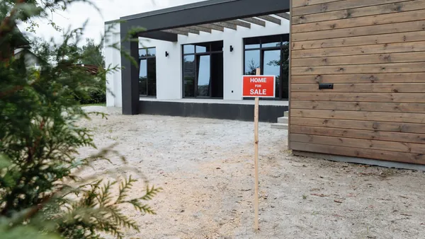A modern house exterior with a small sign in the front yard