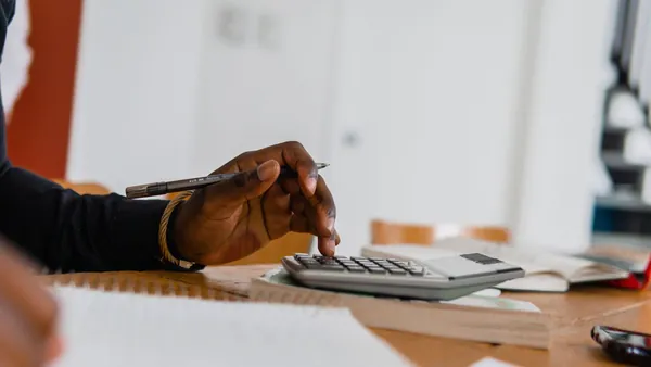 A hand using a calculator beside a pen and paperwork