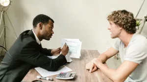 Two people at a table, one showing the other a document